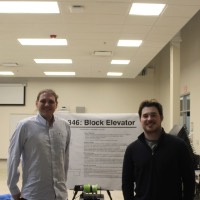 Two students standing next to a second block elevator project.